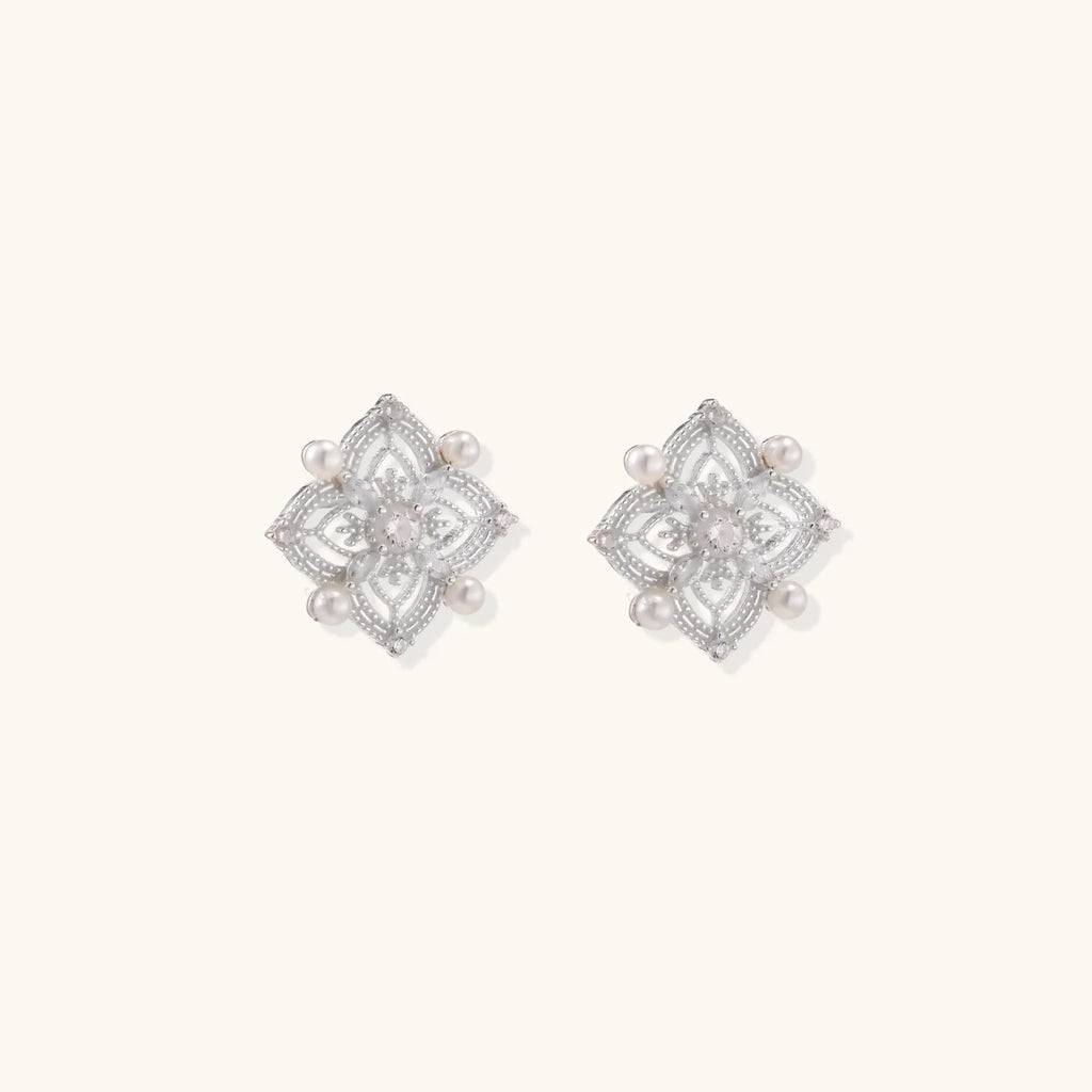 Ornate sterling silver stud earrings with mandala-inspired filigree pattern and four freshwater pearls on beige background